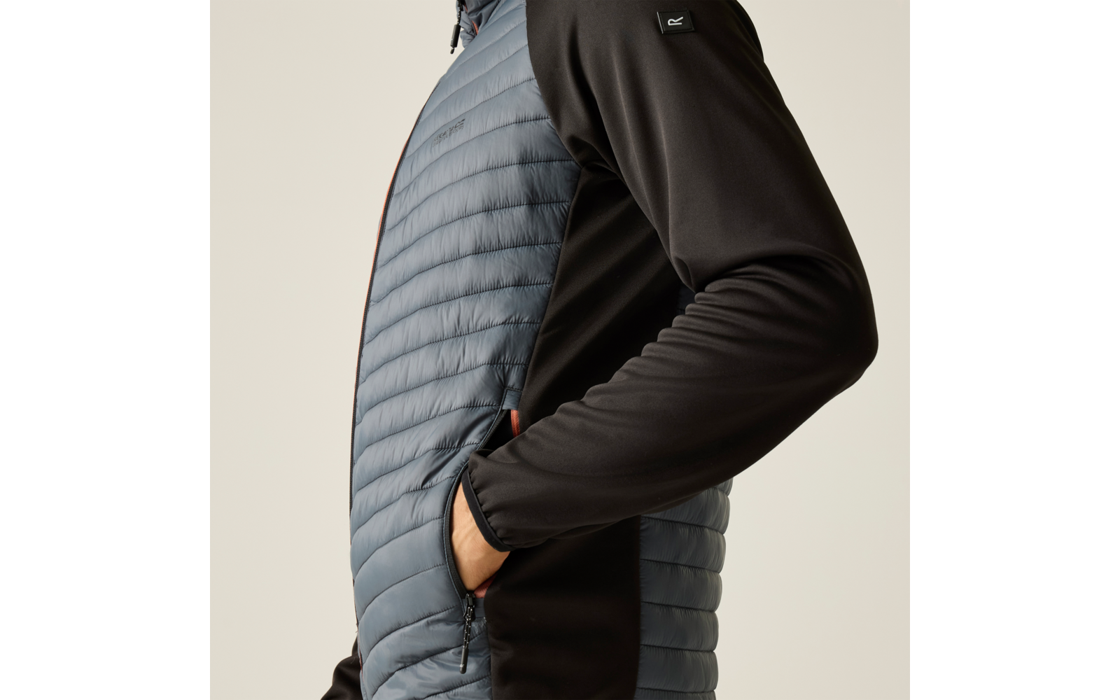 Seitliche Ansicht des Oberkörpers einer Person mit gesteppter hellblauer Front und schwarzen Ärmeln; Hand in seitlicher Reißverschlusstasche