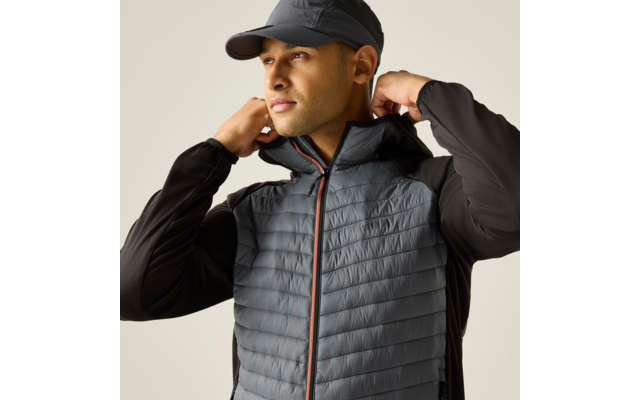 Person mit dunkler Schirmmütze und grauer gesteppter Weste mit Reißverschluss, zieht mit beiden Händen den Kragen hoch und blickt nach links