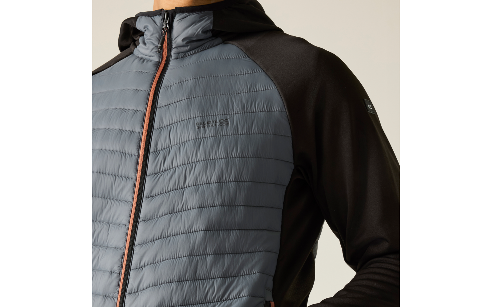 Oberkörper in Kapuzenjacke; gesteppte Vorderseite hellgrau-blau mit horizontalen Nähten, Reißverschluss mit orangefarbener Kante, Ärmel und Seiten schwarz, kleines Logo auf linker Brust