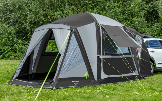 Fahrzeug mit angebautem grauem Vorzelt auf einer grünen Wiese vor Bäumen