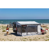 Camping vehicle with awning and two bicycles mounted on its rear on a sandy beach, two people standing nearby, sea on the horizon