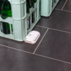 Ein weißer WLAN-Router auf einem dunkelgrauen Fliesenboden neben einem grünen Getränkekasten