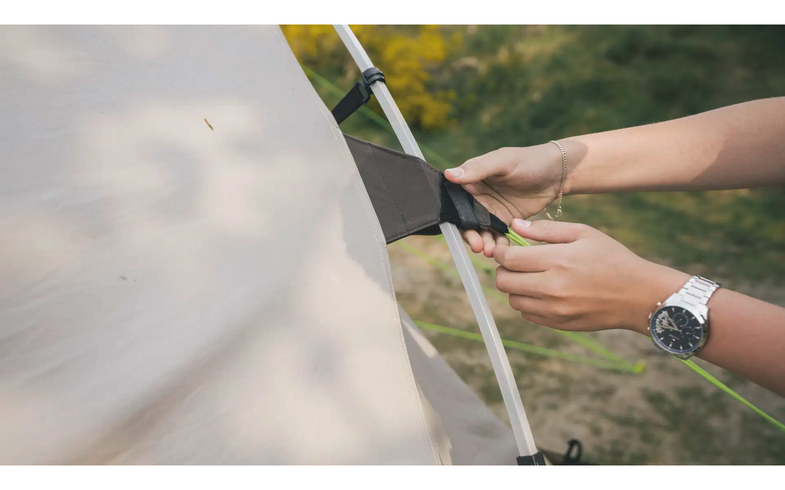 Hände befestigen ein Zelt an einem Gestängebogen