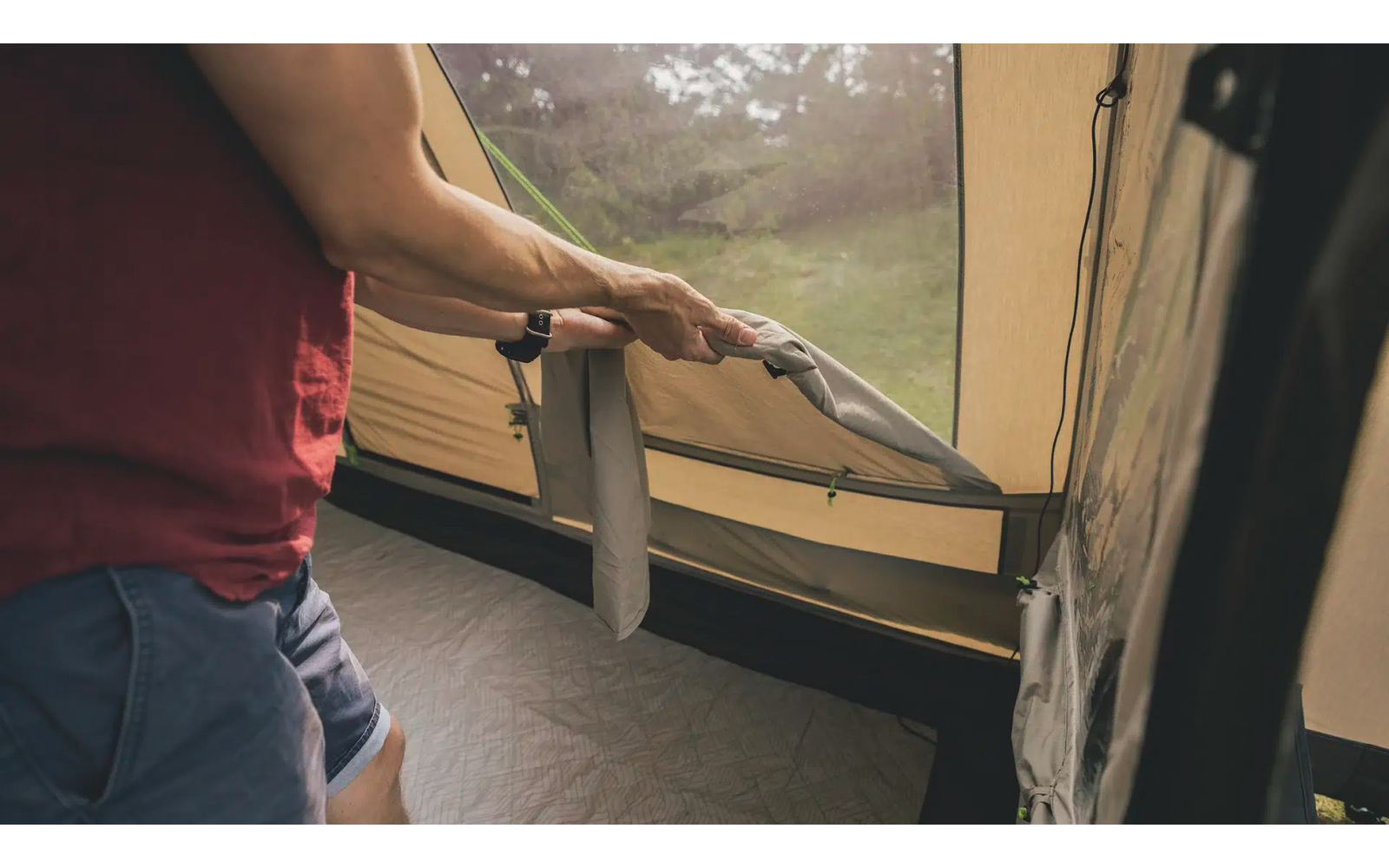 Person im roten Shirt öffnet das Fenster eines Zeltes