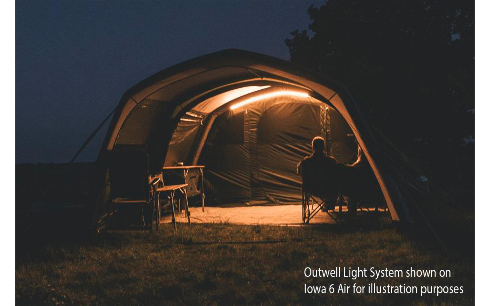 Tente éclairée la nuit, bandes lumineuses à l'intérieur, une personne assise en silhouette devant, table et chaise à l'intérieur, sol herbeux