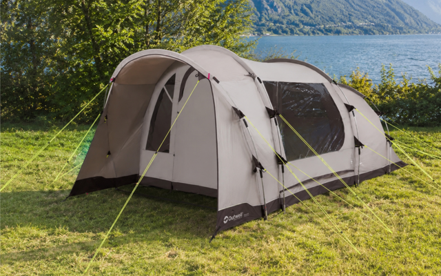 Tente tunnel grise avec haubans visibles sur l'herbe, lac et montagnes en arrière-plan