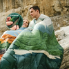 Ein Mann und ein Kind eingehüllt in einen grünen Schlafsack sitzen vor einer Felswand