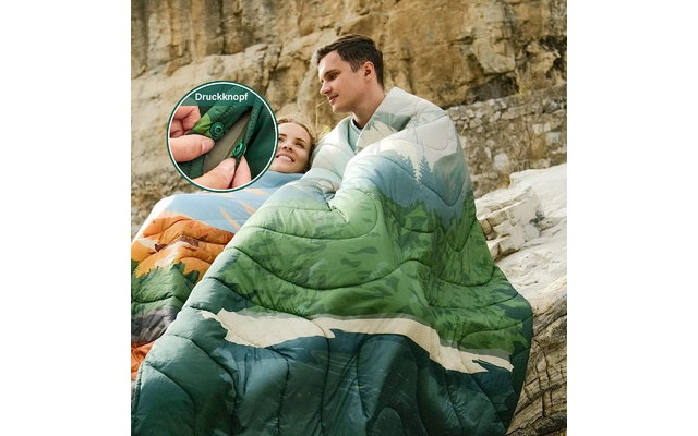 Ein Mann und ein Kind eingehüllt in einen grünen Schlafsack sitzen vor einer Felswand