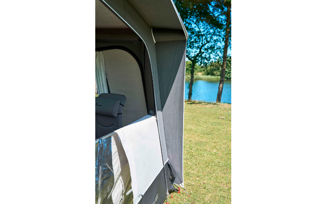 Teil eines grauen Vorzelts mit weiß-transparentem Panel, Gras, ein See und Bäume im Hintergrund, im Inneren ein grauer Campingstuhl