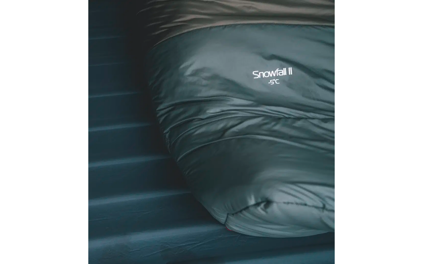 Donkergroene slaapzak met de tekst 'Snapel' op een zwart matras