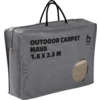 Grijze rechthoekige draagtas met ritssluiting en zwarte handvatten, opdruk "OUTDOOR CARPET NAVA 1.6 X 2.3 M" en ronde uitsnede waar een beige vloerkleed zichtbaar is