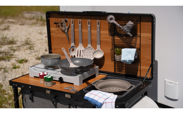 Camping-Kochset mit Pfanne, Geschirr, Besteck und Küchenutensilien auf einem Klapptisch im Freien