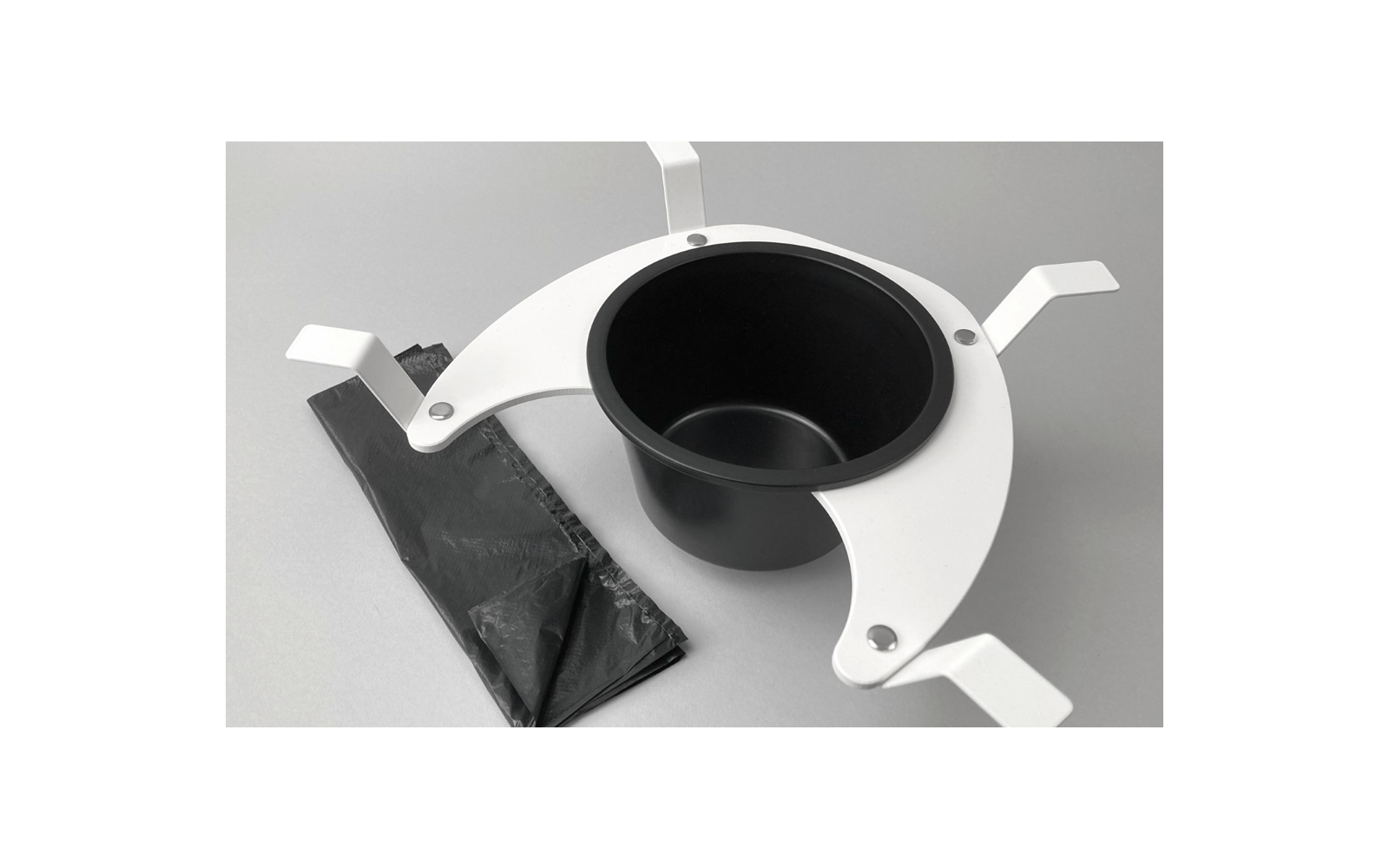Gobelet noir dans un support blanc à trois bras avec un sac plastique noir sur fond gris