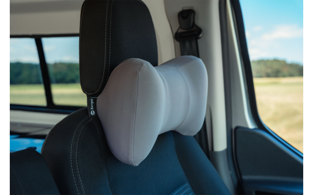 Gray butterfly-shaped neck pillow attached to the headrest of a black car seat; car window showing fields and blue sky