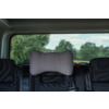 Car rear seat with a gray pillow attached to the middle headrest, black seats, seat belts and blurred trees visible through the rear window