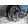 Primer plano de un neumático de coche con cadenas para la nieve, salpicaduras de agua, coche negro y nieve en la carretera