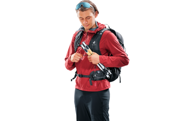 Person mit roter Jacke, schwarzem Rucksack und Sonnenbrille auf dem Kopf, hält zwei Trekkingstöcke vor der Brust und schaut nach unten