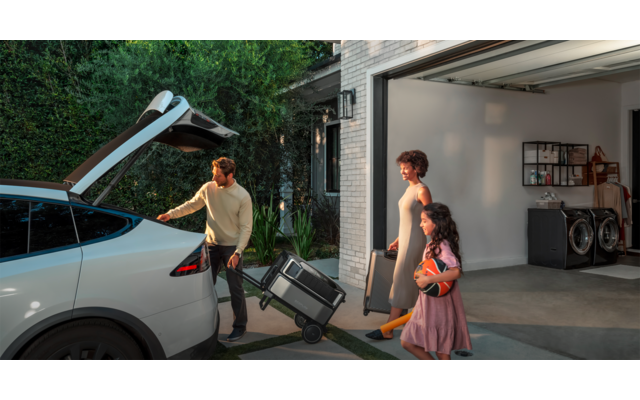 Zwei Personen tragen einen Rollstuhl vom Auto zur Garage