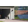 Haus mit geöffnetem Garagentor, Sicht auf Innenraum mit Regal und Koffer, daneben Solarmodule auf dem Boden