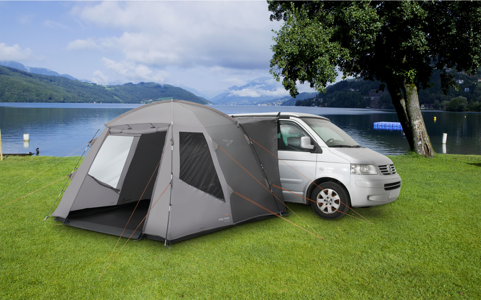 Tent naast een geparkeerde auto op een grasveld bij een meer met bergen op de achtergrond
