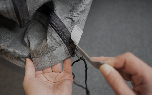 Close-up of two hands pulling a zipper on gray fabric
