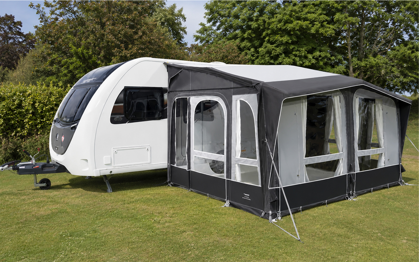 Caravan bianco con veranda grigio scuro su prato verde, alberi sullo sfondo