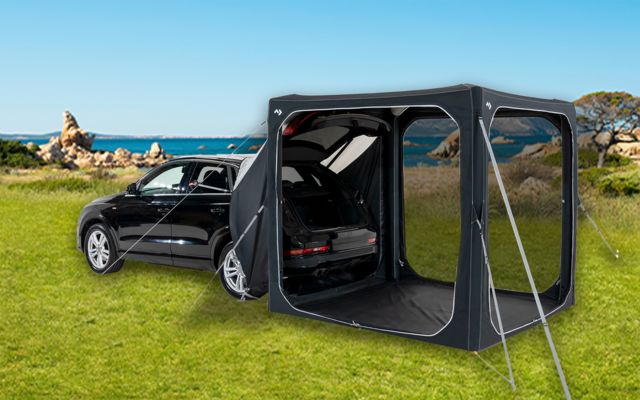 Schwarzes Auto auf einer Wiese mit angebrachtem Zeltvorbau und offenem Kofferraum