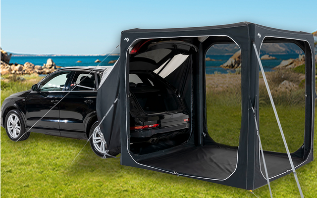 Schwarzes Auto auf einer Wiese mit angebrachtem Zeltvorbau und offenem Kofferraum