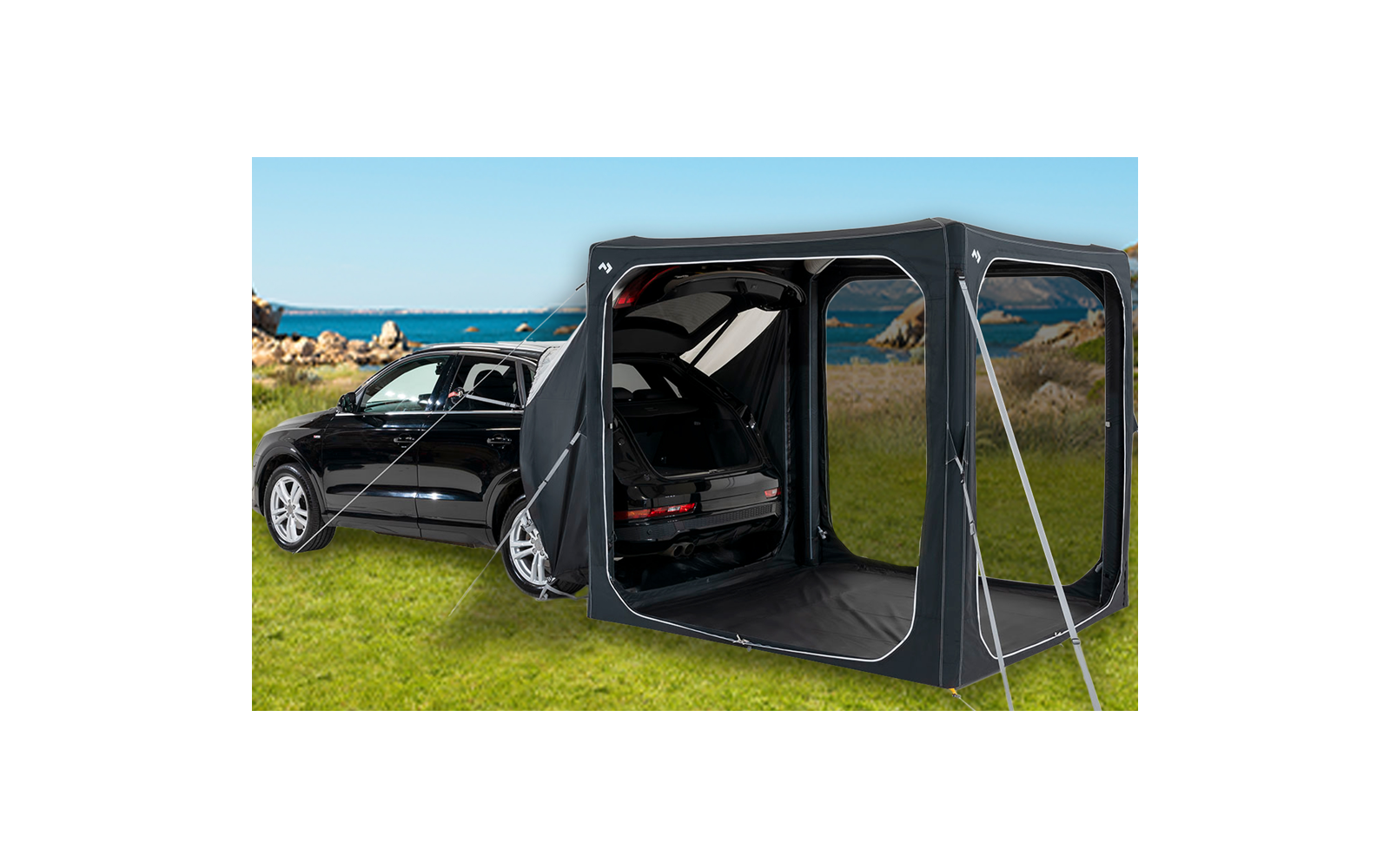 Schwarzes Auto auf einer Wiese mit angebrachtem Zeltvorbau und offenem Kofferraum