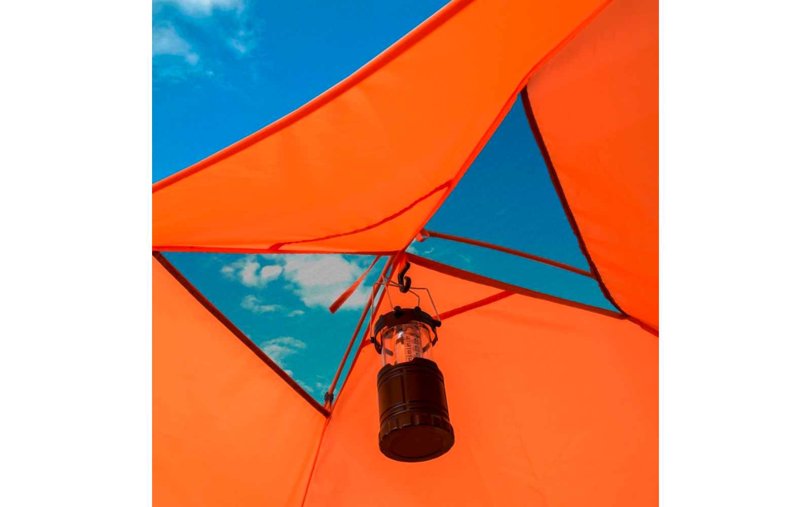 Intérieur d'une tente orange avec des ouvertures triangulaires en résille laissant voir le ciel bleu et des nuages; une lanterne de camping noire pend au centre