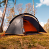 Tente gris foncé, entrée ouverte et intérieur orange, posée sur un sol forestier herbeux entre des arbres fins sous un ciel bleu avec des nuages