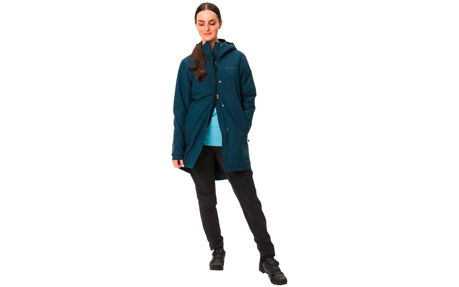 Frau trägt blauen Blazer, schwarzen Rock und schwarze Stiefel, steht vor weißem Hintergrund