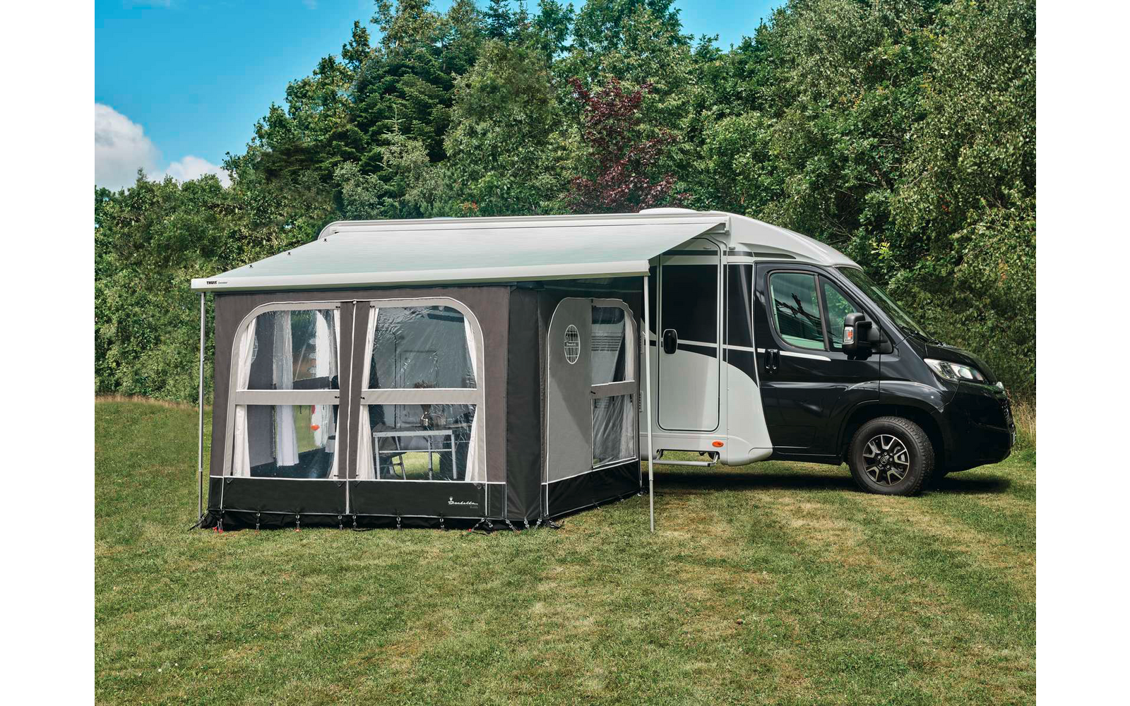 Wohnmobil mit angebautem Vorzelt auf einer Wiese, Bäume und blauer Himmel im Hintergrund