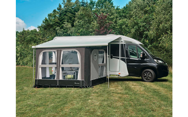 Wohnmobil mit angebautem Vorzelt auf einer Wiese, Bäume und blauer Himmel im Hintergrund