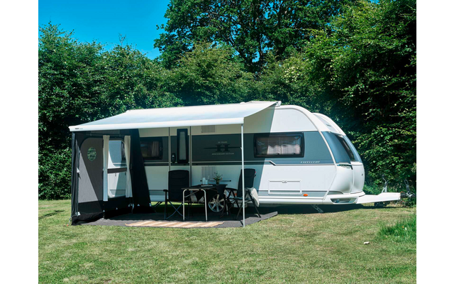 Weißer Wohnwagen mit ausgefahrener Markise, davor Tisch und zwei Stühle auf Rasen, im Hintergrund Bäume
