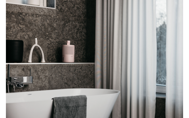 Weißes Badezimmer mit freistehender Badewanne, dunkelgrauen Handtüchern, hellgrauen Wänden und Fenster mit Vorhängen