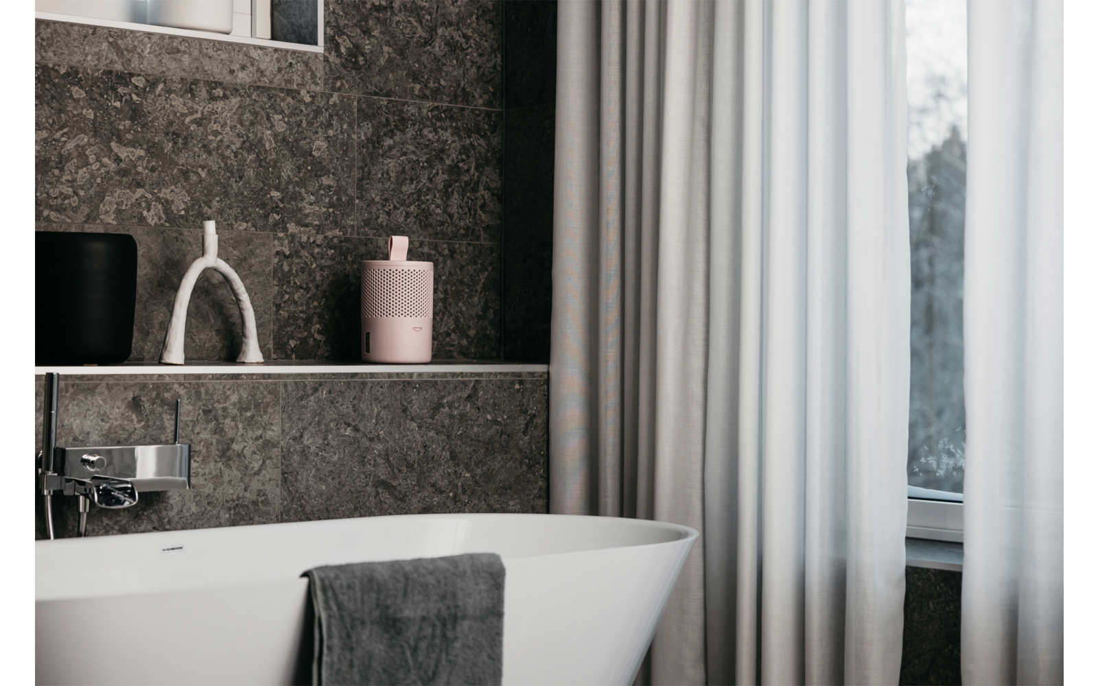 Weißes Badezimmer mit freistehender Badewanne, dunkelgrauen Handtüchern, hellgrauen Wänden und Fenster mit Vorhängen