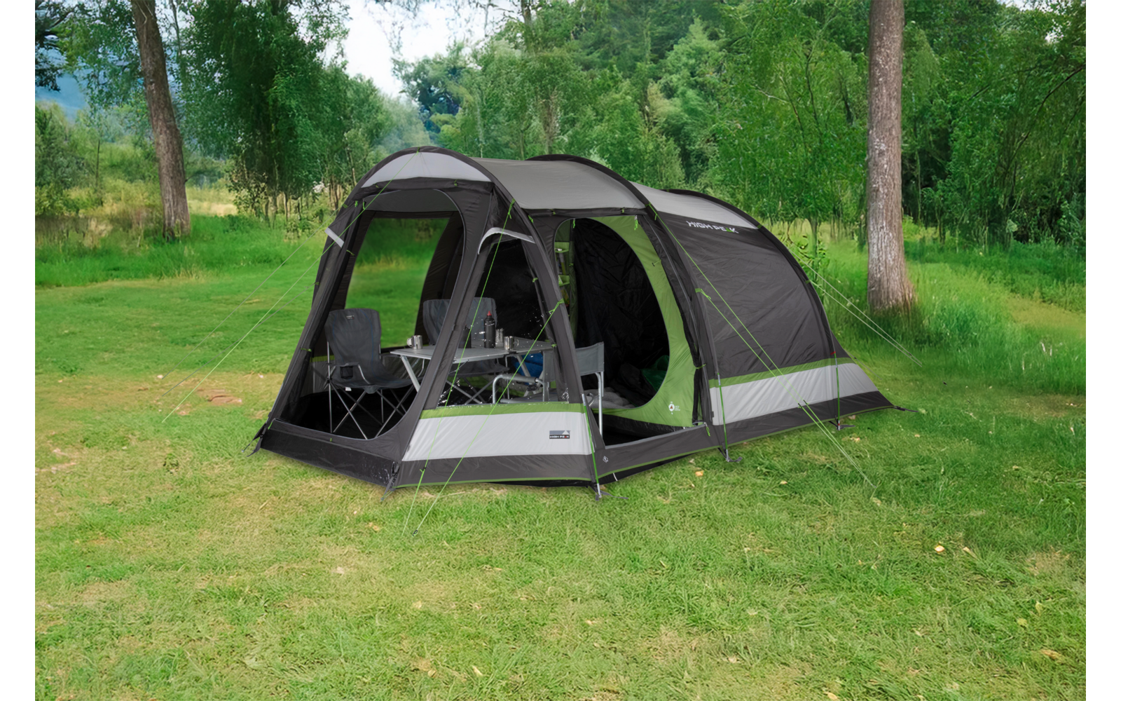 Großes graugrünes Zelt mit Vordach auf Wiese, offene Eingänge, zwei Campingstühle und ein kleiner Klapptisch im Inneren, Bäume im Hintergrund