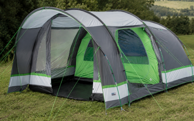 Large gray and green tunnel-style tent with open entrance, side windows, and guy lines staked into grass; treeline in the background