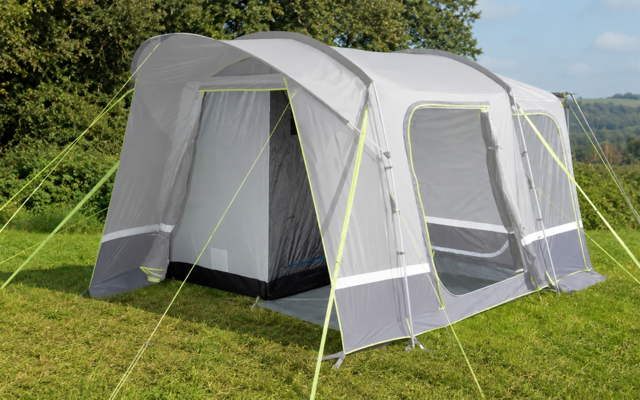 Grijze tent met open ingang en twee grote ramen, gele scheerlijnen, op groen gras voor bomen en heuvels bij licht bewolkte hemel