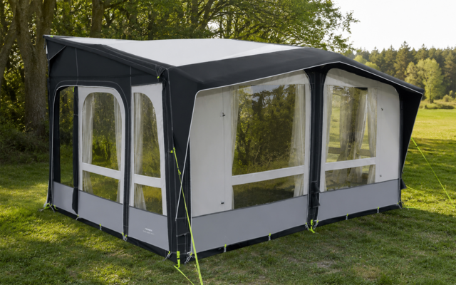 Large gray-and-white tent with several rectangular clear windows on green grass, trees in the background