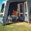 An adult sits in the entrance of a camping awning and leans toward a baby in a stroller