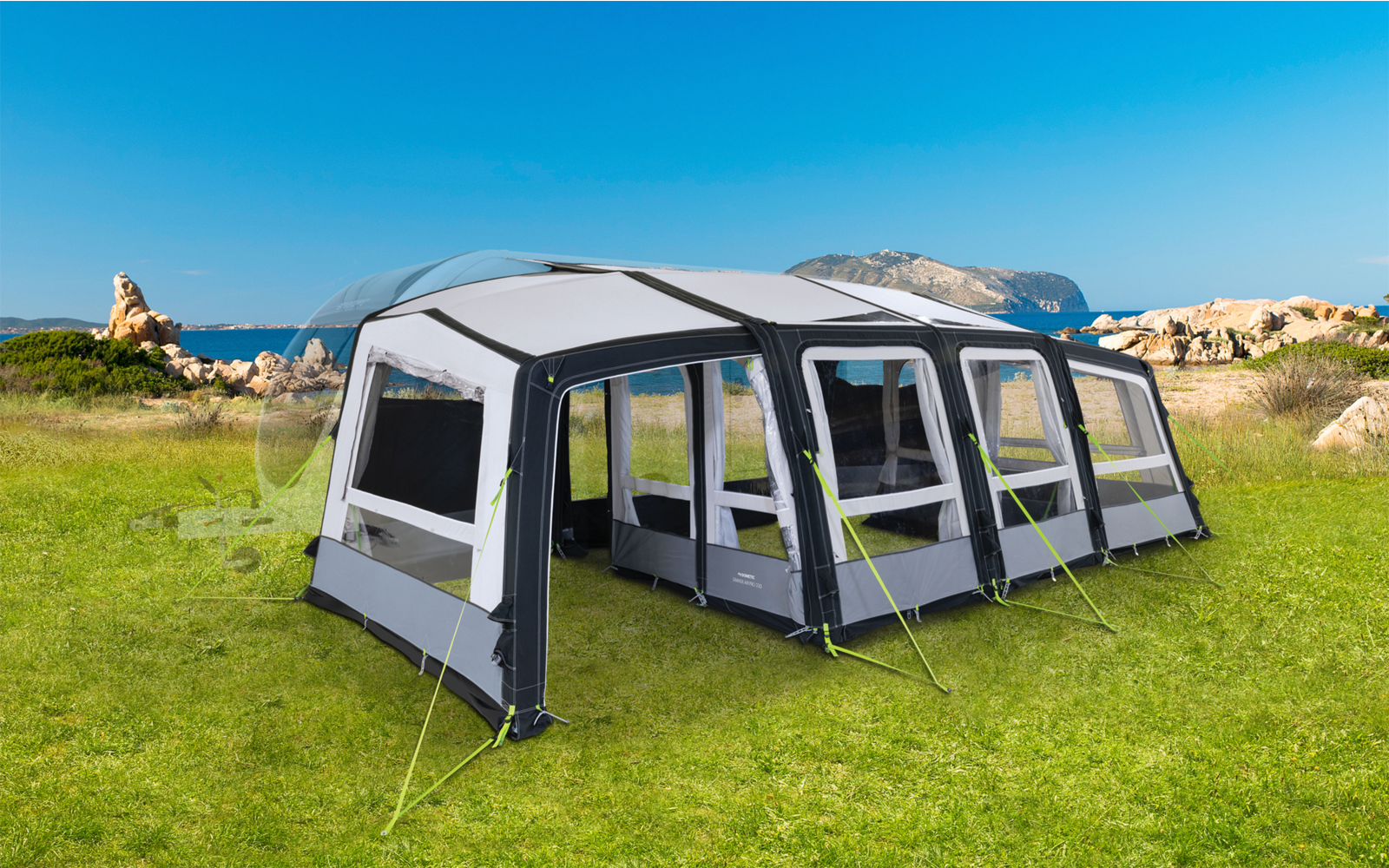 Gran tienda gris con ventanas sobre hierba verde frente a rocas y cielo azul