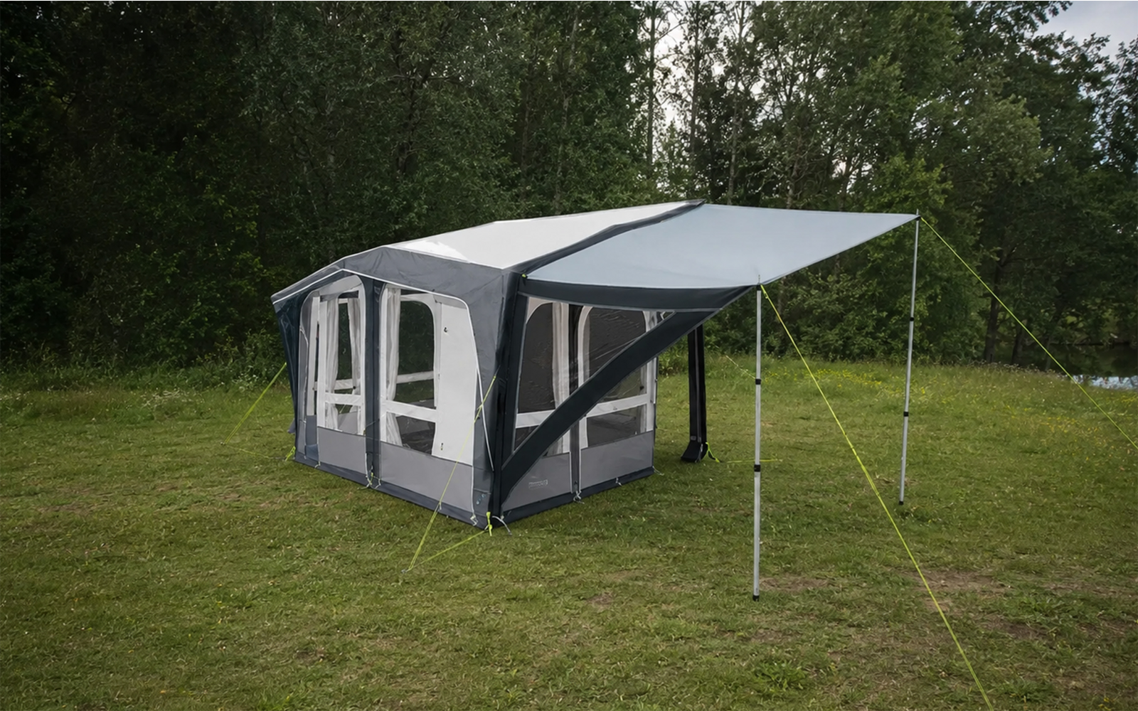 Großes grau-blaues Zelt mit drei sichtbaren Fenstern, ausgeklapptem Vordach, Metallstangen und Abspannleinen auf einer Grasfläche vor Bäumen