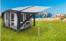 Grijs-witte caravan luifel op groen gras met blauwe lucht en rotsen op de achtergrond
