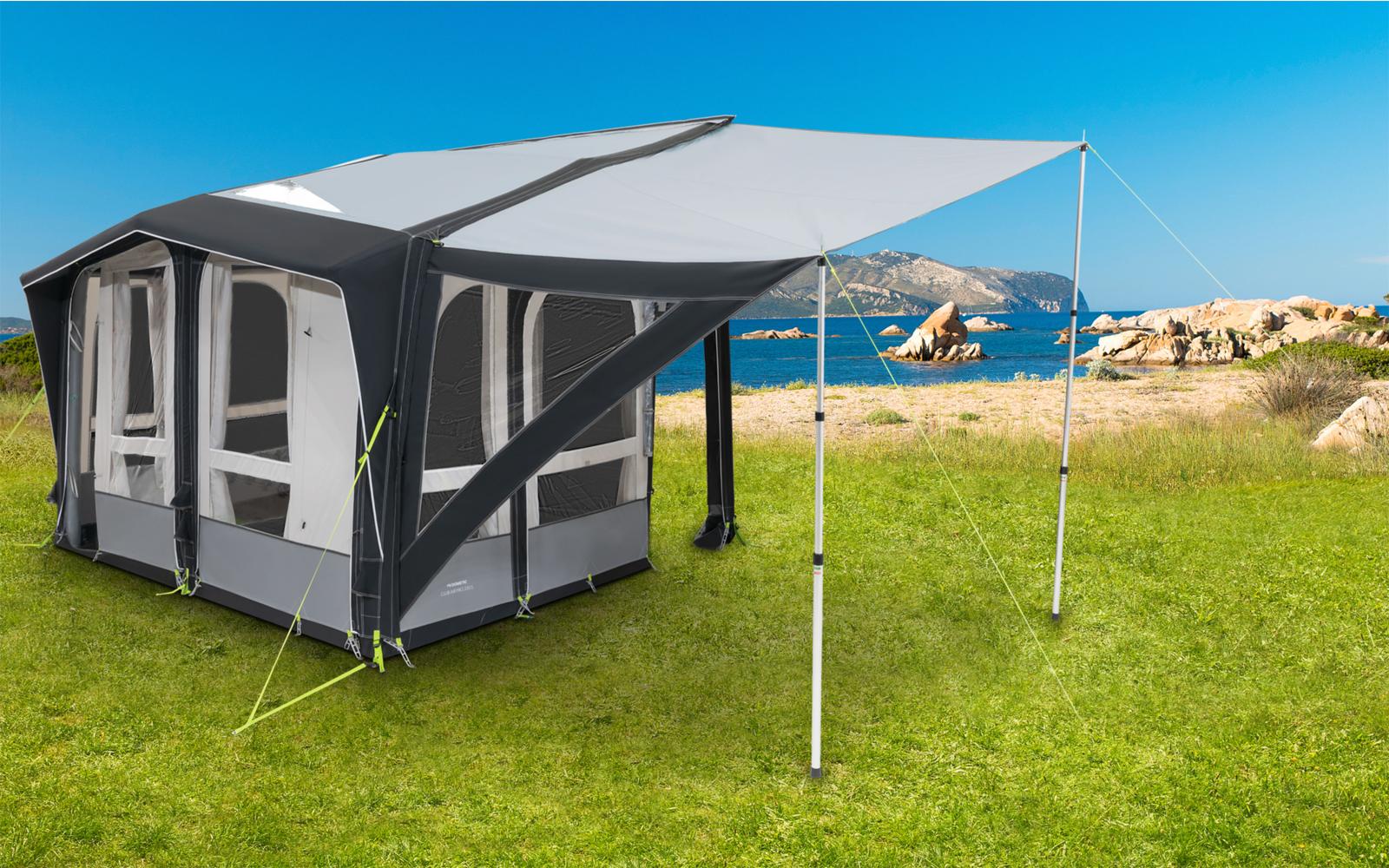 Gray and white caravan awning on green grass with blue sky and rocks in the background