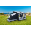 Large black and gray tent on a green meadow with blue sky and rocks in the background