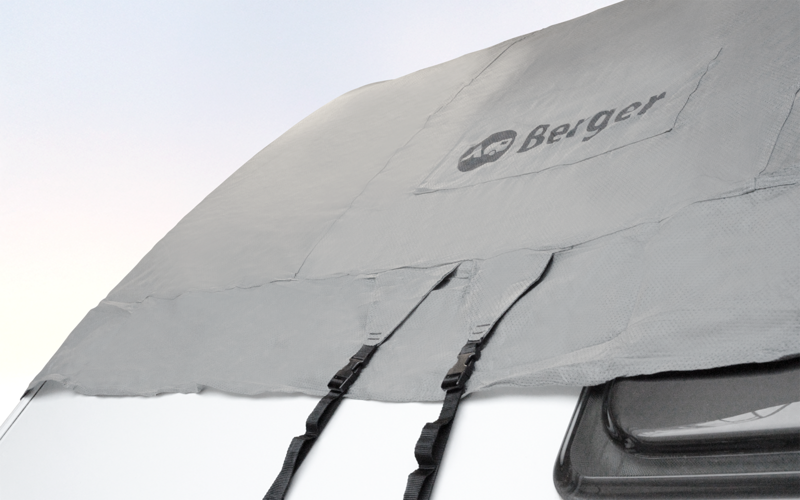 Gray cover with printed logo, two hanging black straps with buckles, a black plastic part at right, pale sky in the background