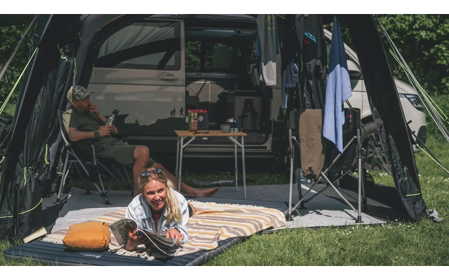 Frau sitzt auf einer Decke vor einem Zelt mit zwei Hunden im Gras