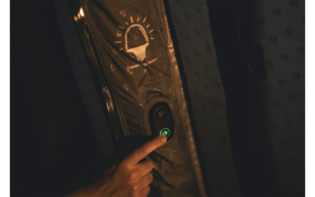 Hand drückt einen grün leuchtenden runden Knopf auf einem vertikalen Panel, darüber ein Glühbirnen-Symbol